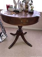 Full view of round mahogany drum table with brown leather inset top, drawer with brass handle, and quadruple base ending in brass claw feet