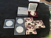 Four commemorative Canadian $1 coins shown: one in a maroon presentation case with a silver coin visible, three others in plastic holders with cardboard sleeves