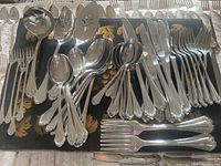 Full view of multiple spoons, forks, and serving pieces laid out on decorative black wood box with floral painting