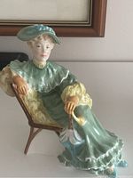 Side view showing seated woman in vintage attire with pale green dress and matching hat, holding closed umbrella.