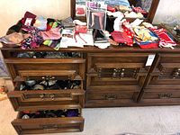 Full view of lot items spread on top of a wooden dresser and inside partially open drawers with belts and scarves visible.
