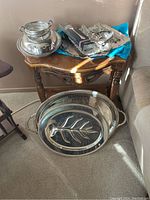Overall lot featuring platters, trays, dishes, and flatware on small table and floor.