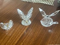 Three Swarovski crystal butterflies displayed on a wood surface, including two with gold antennae and one on frosted leaf base.
