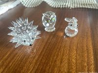 Positioned on a wooden surface with lace doily in background, displaying all three figurines: porcupine, owl, rabbit.