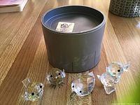 Four clear Swarovski crystal bird and duck figurines displayed beside an original gray round box with Swarovski label inside the lid.