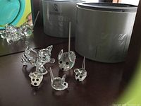 Photo showing one Swarovski crystal cat figurine and four crystal mouse figurines placed on a surface with silver cylindrical boxes in the background.