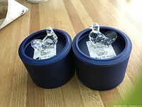 Two clear crystal dove figurines seated in blue round display boxes with original labels beneath.