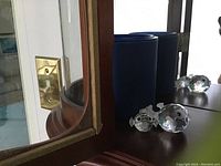 Two Swarovski crystal fish figurines on a wooden surface next to blue boxes and a mirror.