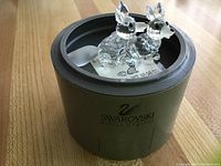 Two Swarovski clear crystal fox figurines inside a black circular box labeled Swarovski Silver Crystal, on wooden surface.