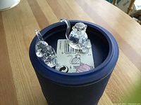 Two clear crystal monkey figurines and one pink crystal ball inside a blue cylindrical Swarovski box.
