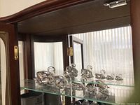 Five Swarovski crystal swan figurines displayed on a glass shelf inside a wooden cabinet, showing graduated sizes.