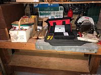 Wide shot of wooden bench holding various tools including boxed items, a tool bag, and wooden storage box with drawers.