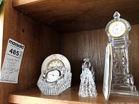 Wooden shelf displaying all four items: Waterford Crystal clock, porcelain floral clock, clear crystal prism clock, and glass angel figurine.