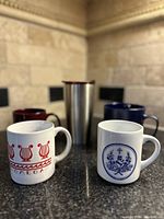 View of two white ceramic mugs with collegiate and fraternity logos and symbols