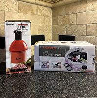 Photo showing two boxed culinary choppers on kitchen counter: a red Geedel Food Chopper and a white Fullstar 4-in-1 Chopper Plus.
