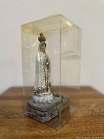 Side angle of the vintage religious statue in a plastic display box showing details of the figure and base.