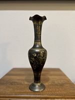 Full view of the tall etched brass vase with floral motifs and scalloped rim on a wooden surface.
