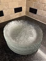 Stack of eight clear glass plates with floral texture viewed from the side showing stacked set.