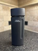 Side view of the dark grey matte stainless steel vacuum tumbler with Nissan branding showing handle indentation and screw-on lid