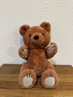 Front view of the brown teddy bear plush showing full body sitting upright with detailed paws and stitched claws.