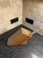 Vintage wooden knife block on countertop with metal kitchen cutter inserted.