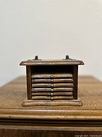 Front view of the wooden coaster holder showing stacked coasters inside with metal knobs on top