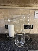 Front view of three clear glass vases of different shapes and one white pillar candle inside medium vase.