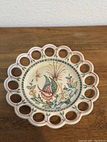 Front of vintage decorative porcelain plate showing hand-painted bird, flowers, and insect with pierced rim design.