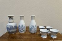 Front view of three hand painted Asian porcelain bottles and four small matching cups with blue floral designs on white porcelain.