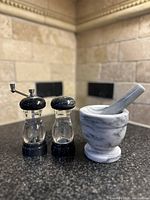 Marble mortar and pestle next to salt and pepper shakers on kitchen counter with a tiled backsplash.