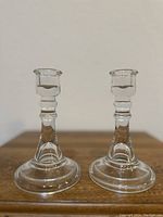 Pair of clear crystal candlestick holders side by side on a wooden surface against a light background.