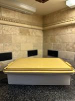 Full view of rectangular Vintage Tupperware cupcake cake container with yellow lid and white base on countertop.