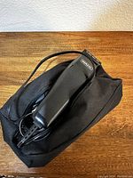 Close-up photo of the Wahl hair clipper and black storage bag on wood surface, showing clipper body, cord and part of storage bag.