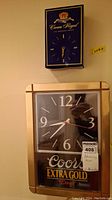 Photo showing both clocks on a wall: Crown Royal clock above and Coors Extra Gold clock below.