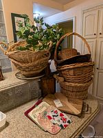 Woven baskets, wooden cutting boards, pot holders, coasters, and faux greenery arranged on a counter.