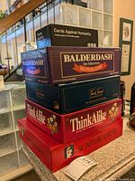 Stacked view showing five game boxes: Cards Against Humanity, Balderdash, Trivial Pursuit, two ThinkAlike, and Scattergories at the bottom.