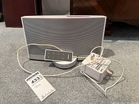 Front view of the white Bose docking station with remote control placed on top of the docking port and power adapter cable visible.