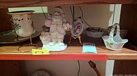 Shelf of Christmas-themed Lenox and other holiday decorative items including Santa figurine, basket dish, planter, and small plates.