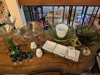 Table display showing green glass vase, small matching glasses, clear etched martini glasses, salt and pepper shakers, condiment tray, and hobnail green glass bowl.