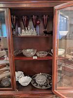 Wide view of wooden cabinet shelves with assorted glassware including crystal, milk glass, and colored etched glasses.