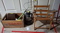 Wooden Kerns Beverages crate, wooden folding chair with damage, black metal lantern, and wire rug beater with green handle shown together.
