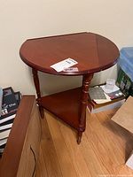 Wooden drop leaf stand with three leaves partly open, visible scratches on surface, triangular lower shelf and turned legs.