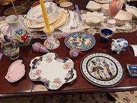 Wide photo showing the Egyptian themed plates, piggy bank, small finger bowl, and other ceramic items on a wooden table.
