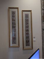Two framed prints hanging on a wall, showing floral designs with gilded decorative frames.