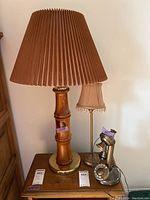 Photo showing vintage rotary dial phone positioned next to wood-based lamp with brown pleated shade and metal-based lamp with small beige beaded shade.