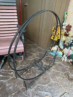 Full side view of black metal round log rack on outdoor stamped concrete floor, showing overall size and shape.