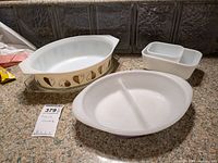 Wide view showing Pyrex casserole dish with brown/gold leaf pattern and lid, two small white food dishes, and a white divided serving dish