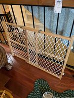 Photo showing wooden framed pet gate with white mesh placed against railing and wall, visible metal latch and hinges.