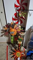 Yard stakes including peppermint swirl circles, autumn leaves with pumpkin center, and nutcracker figure seen in garage setting.