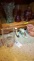 Shelf display showing colored glass decanter, powder jar, glass vase, and three decorative ceramic shoes, one with chips on top